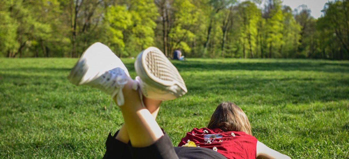 woman in black pants and red shirt lying on green grass field during daytime