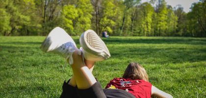 woman in black pants and red shirt lying on green grass field during daytime