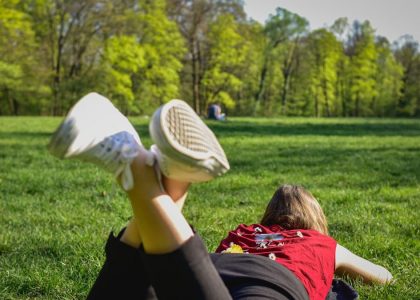 woman in black pants and red shirt lying on green grass field during daytime